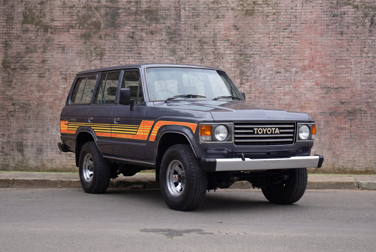 Vintage Toyota SUV with orange stripes parked against a brick wall.