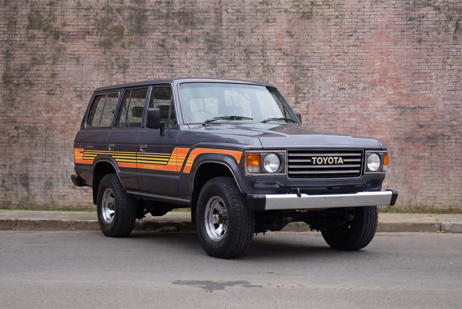 Vintage Toyota SUV with orange stripes parked against a brick wall.